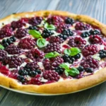 A freshly baked blackberry basil ricotta pizza topped with melted cheese, fresh basil leaves, and juicy blackberries on a wooden board.